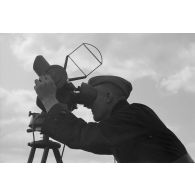Un observateur de la FlaK, scrute le ciel dans un binoculaire monté sur trépied.