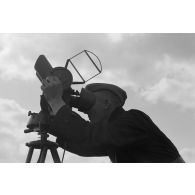 Un observateur de la FlaK, scrute le ciel dans un binoculaire monté sur trépied.