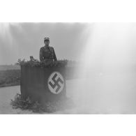 Le Gruppenführer Dr. Otto Zimmermann du N.S.F.K., derrière une tribune, finit un discours et fait le salut nazi (image altérée).