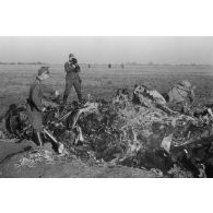 Un policier allemand inspecte des débris d'un avion soviétique abattu, derrière lui un caméraman illustre le sujet pour la propagande.