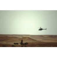 En ZDO (zone de déploiement opérationnel) Olive, un hélicoptère américain de reconnaissance et d'observation Bell-OH58 Kiowa muni d'un système de visée pour la lutte antichar monté sur mat au-dessus du rotor survole un camion du 1er RS (régiment de spahis) posté dans le désert.