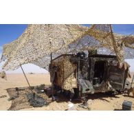 En ZDO (zone de déploiement opérationnel) Olive, un filet de camouflage procure de l'ombre au pied d'un transport de troupes M-113 américain.