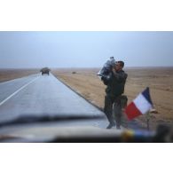 Sur l'axe Texas par un temps pluvieux, un brigadier caméraman de l'ECPA (Etablissement cinématographique et photographique des Armées), caméra sur l'épaule, revient vers le Peugeot P4 sur le capot avant duquel flotte un petit drapeau français.