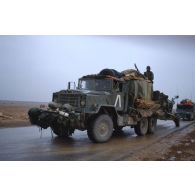 Par un temps pluvieux, un camion américain M939 tractant un obusier de 155 mm M198 passe devant l'objectif sur l'axe Texas.