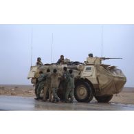 Par un temps pluvieux, un groupe de prisonniers irakiens passe au pied d'un VAB à l'arrêt sur un bas-côté de l'axe Texas, recouvert de filets de camouflage à l'avant et sur les flancs.