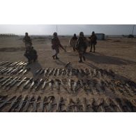 Des armes irakiennes récupérées, fusils d'assaut AK-47 ou AKM, sont alignés au sol aux abords d'Al Salman. En arrière-plan des marsouins du 2e RIMa (régiment d'infanterie de marine) s'affairent à les charger dans une remorque.