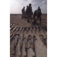 Des armes irakiennes récupérées, fusils d'assaut AK-47 ou AKM, sont alignés au sol aux abords d'Al Salman. En arrière-plan des marsouins du 2e RIMa (régiment d'infanterie de marine) s'affairent à les charger dans une remorque.