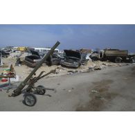 Un canon sans recul irakien SPG 9 abandonné sur le bord d'une route, et en arrière-plan des épaves de voitures civiles détruites.