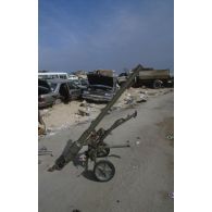 Un canon sans recul irakien SPG 9 abandonné sur le bord d'une route, et en arrière-plan des épaves de voitures civiles détruites.