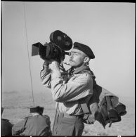 Portrait de Claude Cuny, reporter du Service cinématographique des armées, caméra à la main, lors d'une opération combinée dans le Djebel Amour.