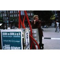 10 juin 1999. Strasbourg (67). Campagne pour les élections européennes. Daniel Cohn-Bendit près de l'affiche annonçant la clôture de la campagne des Verts Place Kléber.