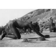 République unie du Cameroun., région de Kaélé, 1949. Femme Guisiga écrasant le mil avec une "Meule" à écraser le mil sur un affleurement rocheux.