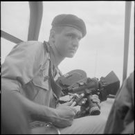 Un sergent, cameraman à l'établissement de la communication de l'armée (E.C.A.), entre deux prises de vues à bord de l'Alouette III.