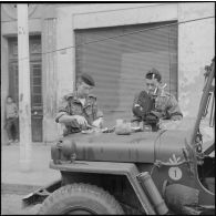Alger. Belcourt. Un soldat et un caméraman du Service cinématographique des armées (SCA) mangent sur le capot d'une jeep pendant les manifestations.