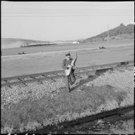 Bône. Manifestations. Un soldat traverse une voie de chemin de fer avec le drapeau du Front de libération national (FLN) dans ses bras.
