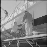 Mers el-Kébir. Les ouvriers repeignent la coque de la vedette côtière P755 à l'aide de panneaux et de rouleaux.