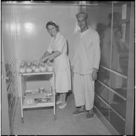 Alger. Clinique du centre hospitalier de la Madeleine. Dans l'ascenseur qui peut contenir deux malades allongés, une infirmière aidée par un malade, descend le matériel nécessaire aux soins du lendemain.