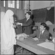 Journée de vote pour le référendum d'autodétermination (1er juillet 1962). Une femme glisse son bulletin de vote dans l'urne face à un assesseur du bureau de vote n°1.