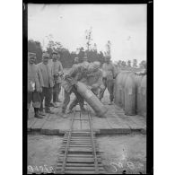 [Des soldats rangent des obus en les faisant rouler à la main sur des rails.]