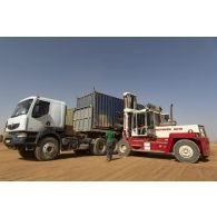 Un chariot élévateur civil charge un container à bord d'un camion semi-remorque en zone logistique de la base de Ménaka, au Mali.
