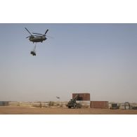 Un chariot élévateur lourd (CEL) charge un container tandis qu'un hélicoptère britannique Chinook CH-47 transporte un véhicule blindé léger (VBL) sur la base de Gao, au Mali.