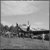 Des habitant d'Attopeu sont rassemblés autour d'un avion posé sur un terrain débroussaillé par la garnison.