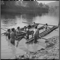 Construction de radeaux pour le transport de paquetages du 2e bataillon de chasseurs laotiens (2e BCL) sur une rivière.