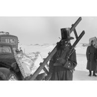 Déguisé en ramoneur, un membre du Sturzkampfgeschwader 2 Immelmann accompagne une affiche qui va accueillir le pilote Rudel.