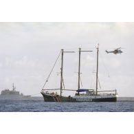 La frégate Vendémiaire (F734) passe aux abords du navire Rainbow Warrior II de l'association Greenpeace, survolé par un hélicoptère Super Puma de l'escadron de transport outre-mer (ETOM) 82 et remorqué par le Rari (A634) après son arraisonnement pour avoir pénétré dans les eaux territoriales françaises et zone interdite autour du site de Mururoa le 9 juillet au matin.