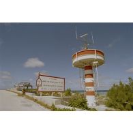 Tour de transmissions au point kilométrique 10 sur l'atoll de Moruroa, et panneau de danger de submersion de la route indiquant "attention, limite de protection du mur, franchissement interdit si feu à éclat en action".