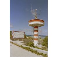 Tour de transmissions au point kilométrique 10 sur l'atoll de Moruroa, et panneau de danger de submersion de la route indiquant "attention, limite de protection du mur, franchissement interdit si feu à éclat en action".