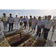 La délégation de membres du gouvernement et d'élus du territoire polynésien visite un ancien puits de tir sur l'atoll de Moruroa. Gaston Flosse, président de la Polynésie française (chemisette bleue), Ismaël Tuahu, maire de Taha'a, et Eugène Bessert, maire de Papara (casquette bleue) sont présents. Un câble de transmissions affleure au sol.