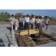 Photographie de groupe de la délégation de membres du gouvernement et d'élus du territoire polynésien devant un ancien puits de tir sur l'atoll de Moruroa. Gaston Flosse, président de la Polynésie française (chemisette bleue), Ismaël Tuahu, maire de Taha'a, et Eugène Bessert, maire de Papara (casquette bleue) sont présents.