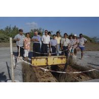 Photographie de groupe de la délégation de membres du gouvernement et d'élus du territoire polynésien devant un ancien puits de tir sur l'atoll de Moruroa. Gaston Flosse, président de la Polynésie française (chemisette bleue), Ismaël Tuahu, maire de Taha'a, et Eugène Bessert, maire de Papara (casquette bleue) sont présents.