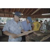 La délégation de membres du gouvernement et d'élus du territoire polynésien visite un atelier d'artisanat tahitien sur l'atoll de Moruroa. Gaston Flosse, président de la Polynésie française, et Eugène Bessert, maire de Papara (au premier plan), examinent des pirogues miniatures et autres objets.