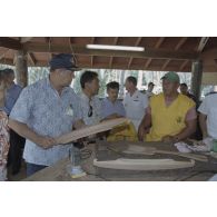 La délégation de membres du gouvernement et d'élus du territoire polynésien visite un atelier d'artisanat tahitien sur l'atoll de Moruroa. Ismaël Tuahu, maire de Taha'a, et Eugène Bessert, maire de Papara (casquette bleue), examinent des pirogues miniatures et autres objets.