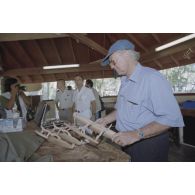 La délégation de membres du gouvernement et d'élus du territoire polynésien visite un atelier d'artisanat tahitien sur l'atoll de Moruroa. Gaston Flosse, président de la Polynésie française (chemisette bleue), examine des pirogues miniatures.