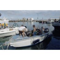 Départ à bord d'un canot du service mixte de surveillance radiologique et biologique (SMSRB) pour une séance de plongée sous-marine de Jean-Jacques de Peretti, ministre de l'Outre-mer. En arrière-plan, d'autres plongeurs du groupe de prélèvements biologiques, et l'adjudant Robaston, caméraman de l'ECPA (tee-shirt vert).