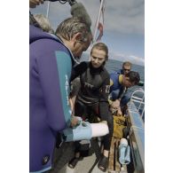 Examen du contrôleur de radioéléments par Jean-Jacques de Peretti, ministre de l'Outre-mer, et Marine Jacquemin, journaliste de TF1, à la remontée de leur plongée sous-marine, à bord du canot du groupe de prélèvements biologiques du service mixte de surveillance radiologique et biologique (SMSRB), dans le lagon de l'atoll de Moruroa.