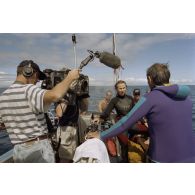 Interview de Jean-Jacques de Peretti, ministre de l'Outre-mer, par Marine Jacquemin, journaliste de TF1, filmée par Benoit Dufeutrelle, caméraman, et Hervé Keraval, preneur de son, de l'équipe de tournage de l'ECPA, à la remontée de leur plongée sous-marine, à bord du canot du groupe de prélèvements biologiques du service mixte de surveillance radiologique et biologique (SMSRB), dans le lagon de l'atoll de Moruroa.