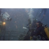 Vue sous-marine pendant la plongée de Jean-Jacques de Peretti, ministre de l'Outre-mer, équipé d'un contrôleur de radioéléments, et de Marine Jacquemin, journaliste de la télévision TF1, avec un caméraman de TF1, sur la tulipe d'un puits de tir d'expérimentation nucléaire sous lagon.