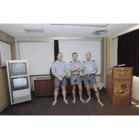 Portrait de personnel de la Marine nationale dans une salle du poste de commandement du groupement opérationnel des essais nucléaires (GOEN) pendant le tir nucléaire Aepytos du 27 octobre 1995. Un comptoir porte l'inscription et l'insigne de la base interarmées (BIA) des sites de Moruroa.