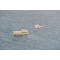 Vue aérienne de l'hélicoptère Super-Puma AS-332 Almée 1 de l’escadron de transport d’Outre-mer (ETOM) de Moruroa en survol de barge d'enregistrement et de mesure MTCT02 du commissariat à l'énergie atomique (CEA) lors du cinquième tir Thémisto de la dernière série des essais nucléaires français dans le lagon de l'atoll de Moruroa.