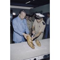 Visite de la boulangerie sur l'atoll de Moruroa. Charles Hernu, ministre de la Défense, goûte une baguette de pain aux côtés du général de corps d’armée aérienne Michel Rouyer, directeur des centres d'expérimentations nucléaires (DIRCEN).