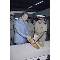 Visite de la boulangerie sur l'atoll de Moruroa. Charles Hernu, ministre de la Défense, goûte une baguette de pain aux côtés du général de corps d’armée aérienne Michel Rouyer, directeur des centres d'expérimentations nucléaires (DIRCEN).