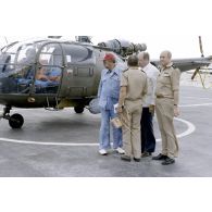 A l'héliport en zone aéroportuaire de l'atoll de Moruroa, Charles Hernu, ministre de la Défense, discute avec le général de corps d’armée aérienne Michel Rouyer, directeur des centres d'expérimentations nucléaires (DIRCEN) et des membres de sa délégation, devant un hélicoptère de reconnaissance Alouette III.