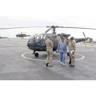 A l'héliport en zone aéroportuaire de l'atoll de Moruroa, Charles Hernu, ministre de la Défense, discute avec le général de corps d’armée aérienne Michel Rouyer, directeur des centres d'expérimentations nucléaires (DIRCEN) et des membres de sa délégation, devant un hélicoptère de reconnaissance Alouette III.