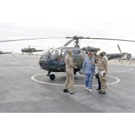 A l'héliport en zone aéroportuaire de l'atoll de Moruroa, Charles Hernu, ministre de la Défense, discute avec le général de corps d’armée aérienne Michel Rouyer, directeur des centres d'expérimentations nucléaires (DIRCEN) et des membres de sa délégation, devant un hélicoptère de reconnaissance Alouette III.