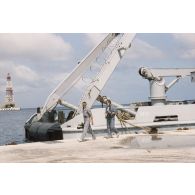 L'adjudant Serge Duponcel, caméraman, et le militaire du rang Emmanuel Ferrat, preneur de son, de l'équipe de tournage de l'ECPA devant le remorqueur-ravitailleur Revi (A635) au port de l'atoll de Moruroa. En arrière-plan, la plateforme Tila.