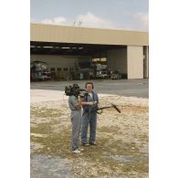 L'adjudant Serge Duponcel, caméraman, et le militaire du rang Emmanuel Ferrat, preneur de son, de l'équipe de tournage de l'ECPA à l'aéroport de l'atoll de Moruroa. En arrière-plan, deux hélicoptères Super Puma au hangar.